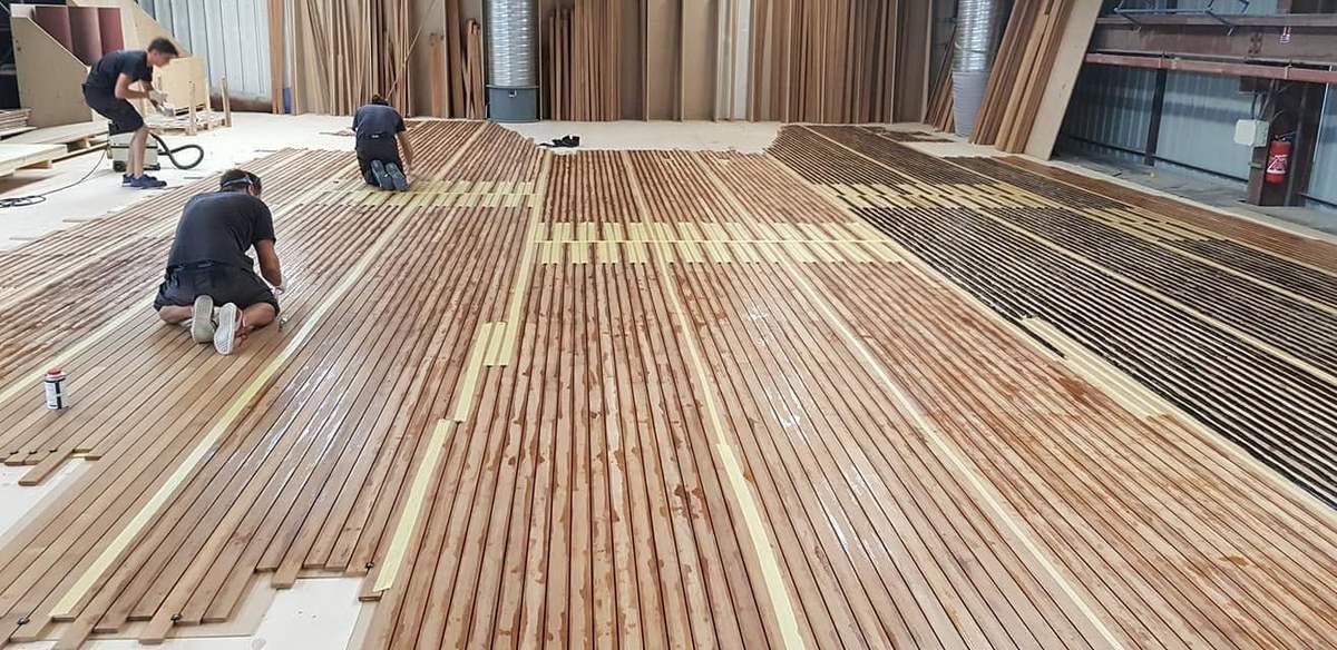 Deck fitters laying solid teak planks during fabrication